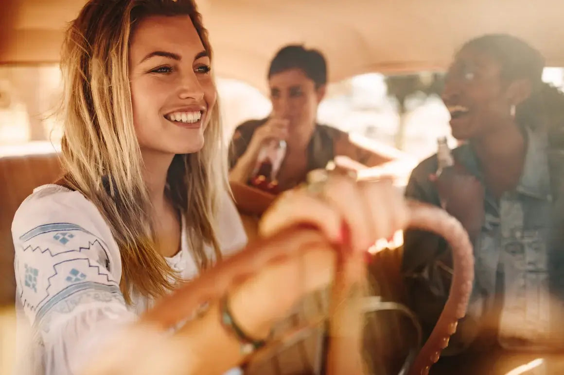 Happy friends driving in a car on a road trip.