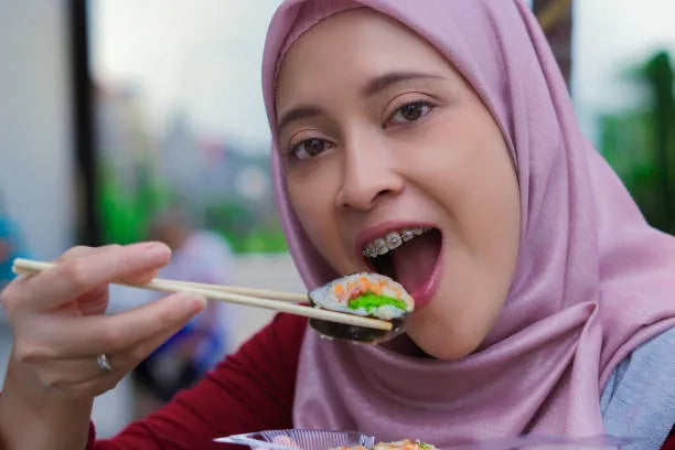 Person eating sushi with chopsticks, smiling with braces