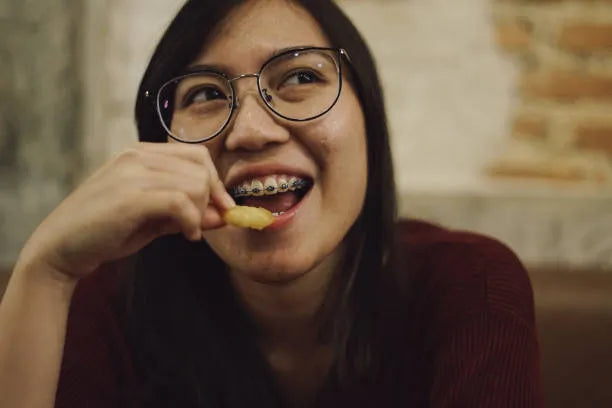 Smiling teen with braces enjoying soft foods like chicken nuggets