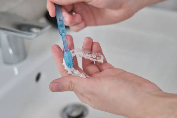 A person brushing their clear brace with a toothbrush in a bathroom setting, focusing on oral hygiene