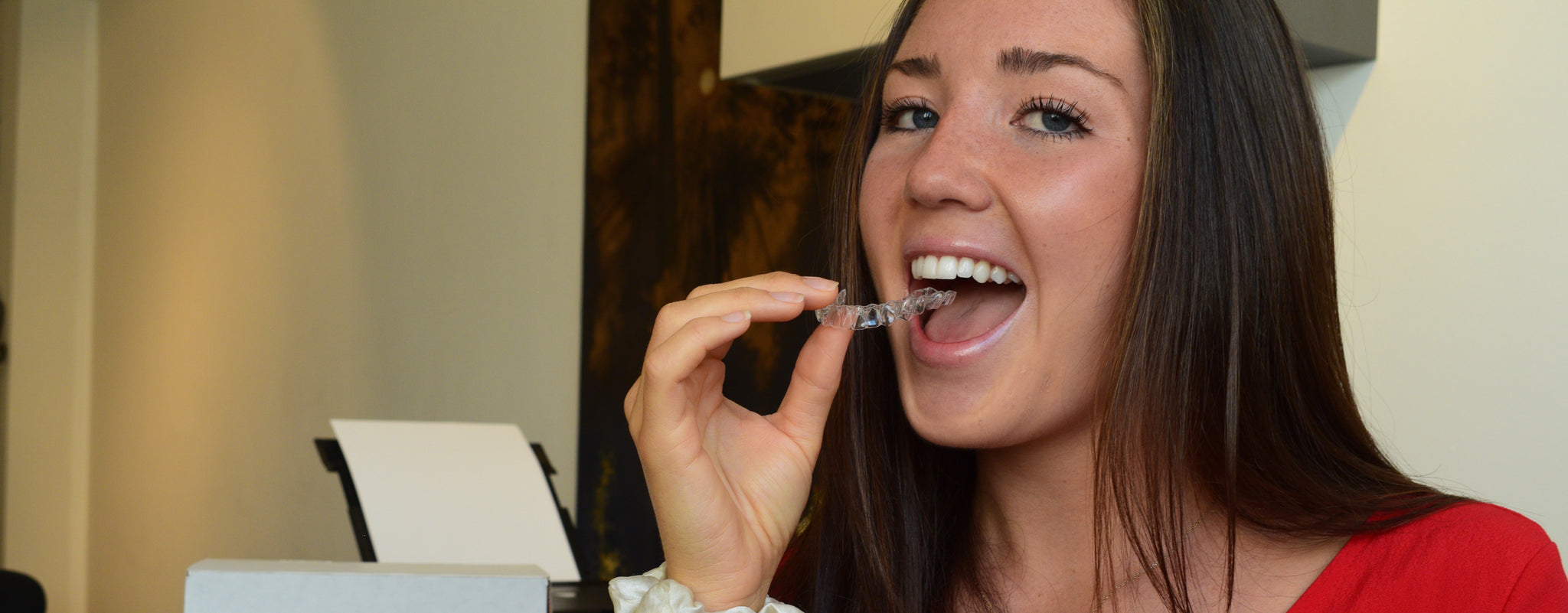 Woman holding clear aligner next to her open mouth.
