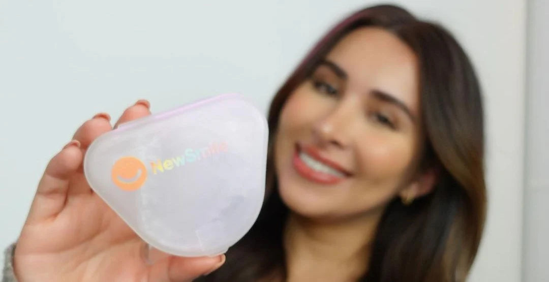 A smiling woman holds up a clear, heart-shaped case with the "NewSmile" logo visible.